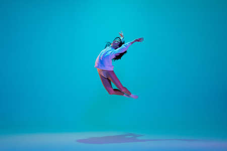 Flying. Young and graceful ballet dancer isolated on blue studio background in neon light. Art,...