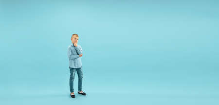 Thoughtful. Childhood and dream about big and famous future. Pretty little boy isolated on blue studio background. Childhood, dreams, imagination, education, facial expression, emotions concept. Flyerの写真素材