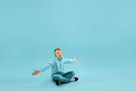 Astonished. Childhood and dream about big and famous future. Pretty little boy isolated on blue studio background. Childhood, dreams, imagination, education, facial expression, emotions concept.の写真素材