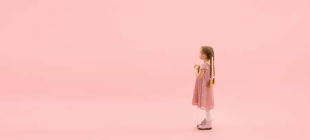 Hopeful. Childhood and dream about big and famous future. Pretty longhair girl on coral pink studio background. Childhood, dreams, imagination, education, facial expression, emotions concept. Flyerの写真素材