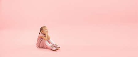Dreamful baby. Childhood and dream about big and famous future. Pretty girl on coral pink studio background. Childhood, dreams, imagination, education, facial expression, emotions concept. Flyerの写真素材