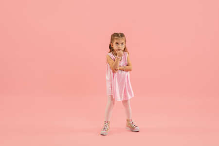 Thinking. Childhood and dream about big and famous future. Pretty longhair girl on coral pink studio background. Childhood, dreams, imagination, education, facial expression, emotions concept.の写真素材