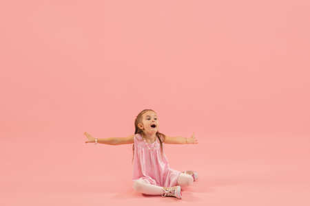 Crazy happy, astonished. Childhood, dream about big and famous future. Pretty longhair girl on coral studio background. Childhood, dreams, imagination, education, facial expression, emotions concept.の写真素材