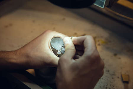 Leveling. Close up hands of jeweller, goldsmiths making of golden ring with gemstone using professional tools. Craft production, precious and luxury jewel, hand made occupation. Workshop, artwork.の写真素材