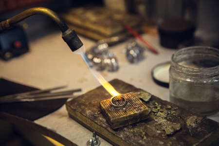 Heating. Close up hands of jeweller, goldsmiths making of silver ring with gemstone using professional tools. Craft production, precious and luxury jewel, hand made occupation. Workshop, artwork.の写真素材
