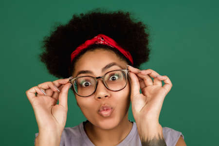 Funny. African-american beautiful womans portrait isolated on green studio background with copyspace. Female model with eyewear. Concept of human emotions, facial expression, sales, ad, fashion.の写真素材