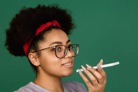 Voice message. African-american beautiful womans portrait isolated on green studio background with copyspace. Female model with phone. Concept of human emotions, facial expression, sales, ad, fashion.の写真素材
