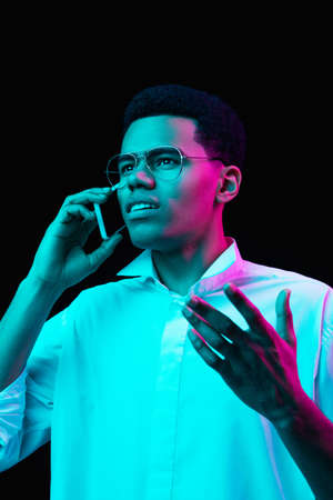 Phone talking. African-american mans portrait on black studio background in multicolored neon light....