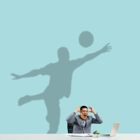 Young asian man dreaming about future in big sport during his work in office. Becoming a legend. Shadow, silhouette of professional football player on the wall. Inspiration, aspiration. Copyspace.の写真素材