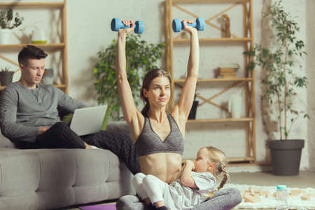 Workout with daughter. Young woman exercising fitness, aerobic, yoga at home, sporty lifestyle and home gym. Getting active during lockdown, quarantine. Healthcare, movement, wellness concept.の写真素材