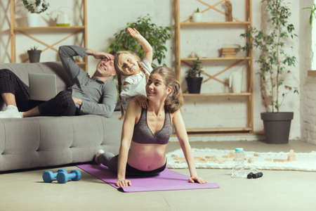 Doing yoga with daughter. Young woman exercising fitness, aerobic, yoga at home, sporty lifestyle...