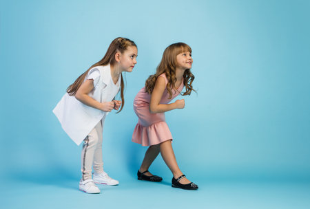 Happy kids, girls isolated on blue studio background. Look happy, cheerful. Copyspace for ad. Childhood, education, emotions, business, facial expression concept. Ready to run, start upの写真素材