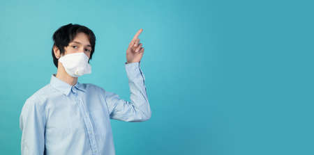 Pointing. Man in protective face mask isolated on blue studio background.の写真素材