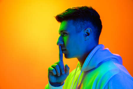 Secret. Caucasian mans portrait isolated on yellow studio background in mixed neon light. Handsome male model. Concept of human emotions, facial expression, sales, ad, fashion. Copyspace.の写真素材