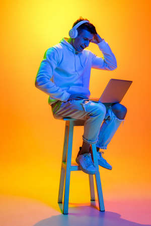 Typing on laptop with headphones. Caucasian mans portrait isolated on yellow studio background in...