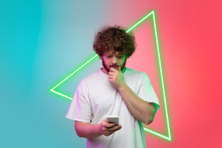 Caucasian young mans portrait isolated on gradient blue-red studio background in neon light with glowing triangle. Looks futuristic. Concept of human emotions, facial expression, sales, ad.の写真素材