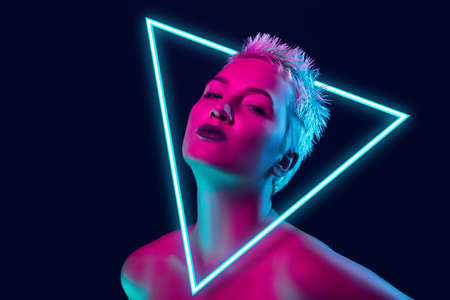 Future. Portrait of female fashion model in neon light with neoned blue glowing triangle on dark studio background. Beautiful woman with trendy make-up and well-kept skin. Vivid style, beauty concept.の写真素材