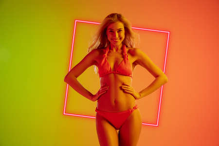 Fashion portrait of young fit and sportive caucasian woman in stylish swimwear on gradient background with pink neoned square. Perfect body ready for summertime. Beauty, resort, sport concept.の写真素材