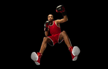 Young african-american professional boxer in action, motion isolated on black background, look from the bottom. Concept of sport, movement, energy and dynamic, healthy lifestyle. Training, practicing.の写真素材