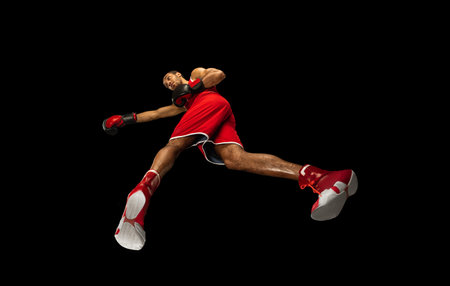 Young african-american professional boxer in action, motion isolated on black background, look from...