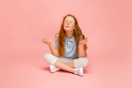 Balanced, calming down. Happy, smiley redhair girl isolated on pink studio background with copyspace...