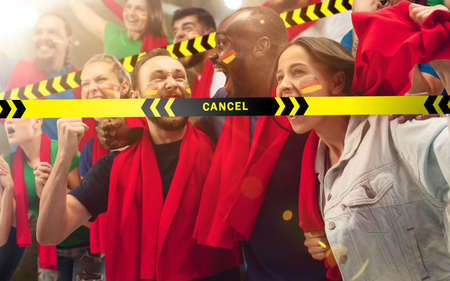 Lockdown. Germanian soccer, football fans cheering for favourite sport team with bright emotions behind the limiting tapes with Cancel. Look excited, supporting, wondered. Blocked social life.の写真素材