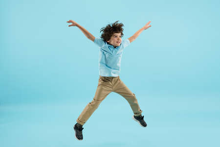 Flying, jumping high. Childhood and dream about big and famous future. Pretty little boy isolated on blue studio background. Dreams, imagination, education, facial expression, emotions concept.の写真素材