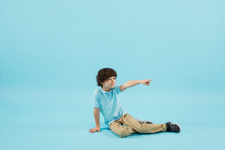 Pointing out, showing. Childhood and dream about big and famous future. Pretty little boy isolated on blue studio background. Dreams, imagination, education, facial expression, emotions concept.の写真素材