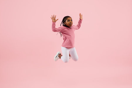Jumping, flying. Childhood and dream about big and famous future. Pretty little girl isolated on coral pink studio background. Dreams, imagination, education, facial expression, emotions concept.の写真素材