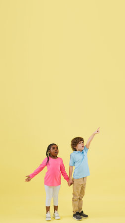 Pointing, flyer. Childhood and dream about big and famous future. Pretty little kids isolated on yellow studio background. Dreams, imagination, education, facial expression, emotions concept.の写真素材