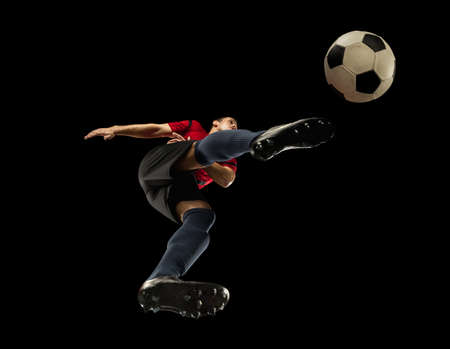 Young caucasian football, soccer player in action, motion isolated on black background, look from the bottom. Concept of sport, movement, energy and dynamic, healthy lifestyle. Training, practicing.の写真素材