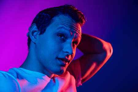 Caucasian mans portrait on purple blue studio background in multicolored neon light. Beautiful male model. Concept of human emotions, facial expression, sales, ad, fashion. Copyspace.の写真素材