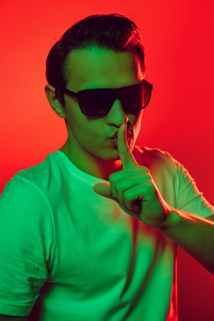 Caucasian mans portrait isolated on red studio background in multicolored neon light. Beautiful male model. Concept of human emotions, facial expression, sales, ad, fashion. Copyspace.の写真素材