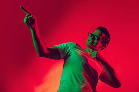 Stylish. Caucasian mans portrait isolated on red studio background in multicolored neon light....