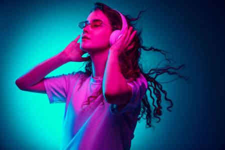 Dancing. Caucasian womans portrait isolated on blue studio background in multicolored neon light....
