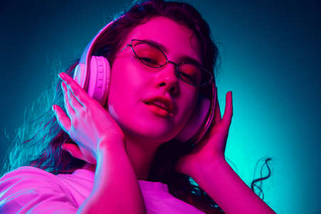 Dancing. Caucasian womans portrait isolated on blue studio background in multicolored neon light. Beautiful female model. Concept of human emotions, facial expression, sales, ad, fashion. Copyspace.の写真素材