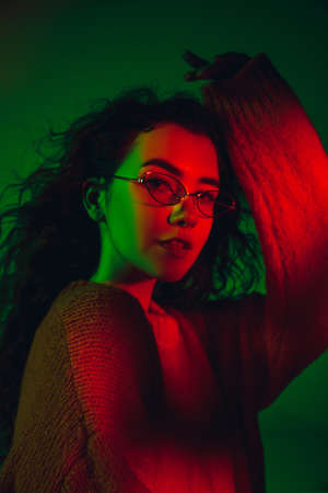 Street style. Caucasian womans portrait on green studio background in multicolored neon light....