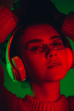 Party. Caucasian womans portrait isolated on green studio background in multicolored neon light. Beautiful female model. Concept of human emotions, facial expression, sales, ad, fashion. Copyspace.の写真素材