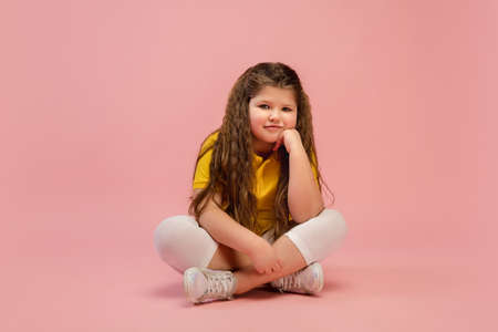Thinking. Happy, smiley little caucasian girl isolated on coral pink studio background with...
