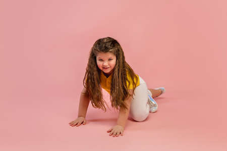 Energy. Happy, smiley little caucasian girl isolated on coral pink studio background with copyspace for ad. Looks happy, cheerful. Childhood, education, human emotions, facial expression concept.の写真素材