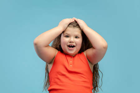 Shocked. Happy, smiley little caucasian girl isolated on blue studio background with copyspace for ad. Looks happy, cheerful. Childhood, education, human emotions, facial expression concept.の写真素材