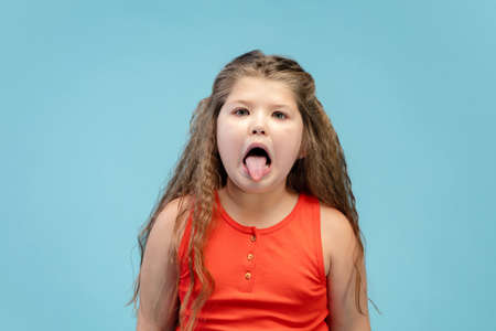 Gremaces. Happy, smiley little caucasian girl isolated on blue studio background with copyspace for ad. Looks happy, cheerful. Childhood, education, human emotions, facial expression concept.の写真素材