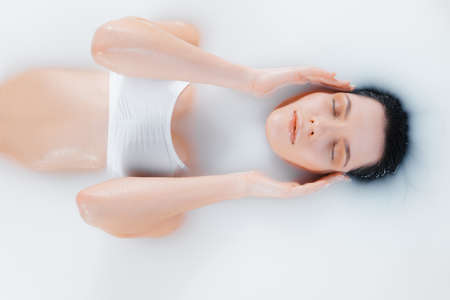 Beautiful female brunette model in milk bath with soft white glowing. Copyspace for advertising....