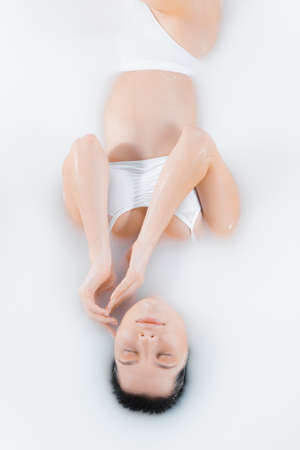 Beautiful female brunette model in milk bath with soft white glowing. Copyspace for advertising....