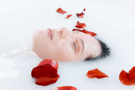 Close up female face in the milk bath with soft white glowing and rose petals. Copyspace for...