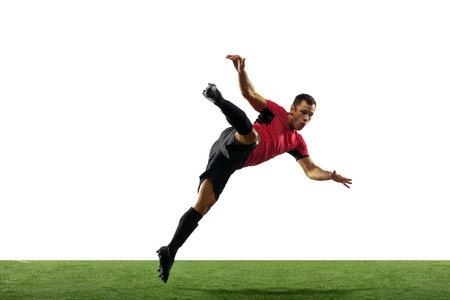 Powerful, flying above the field. Young football, soccer player in action, motion isolated on white background with green grass. Concept of sport, movement, energy and dynamic, healthy lifestyle.の写真素材