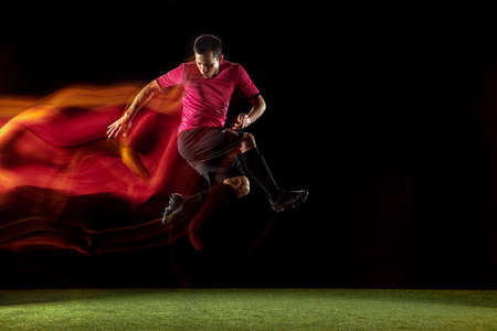 Powerful, flying above the field. Young football, soccer player in action, motion on black...