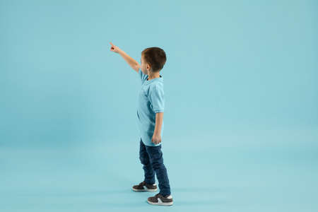 Pointing. Childhood and dream about big and famous future. Pretty little boy isolated on blue studio background. Dreams, imagination, education, facial expression, emotions concept.の写真素材