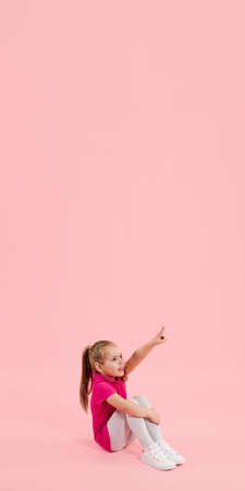 Pointing. Childhood and dream about big and famous future. Pretty little girl isolated on coral pink studio background. Dreams, imagination, education, facial expression, emotions concept. Flyerの写真素材