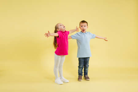 Greeting, showing. Childhood and dream about big and famous future. Pretty little kids isolated on yellow studio background. Dreams, imagination, education, facial expression, emotions concept.の写真素材